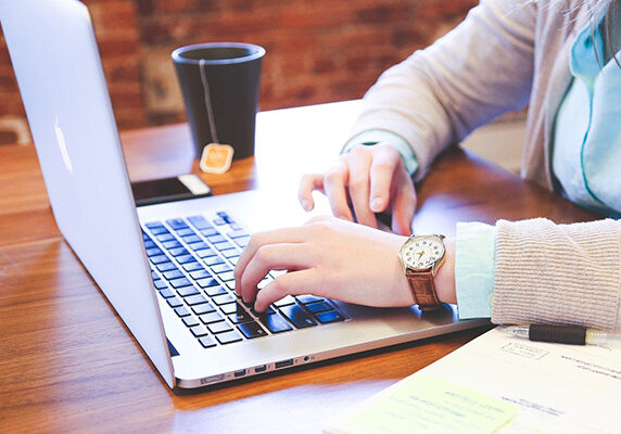 person searching on laptop with cup of tea